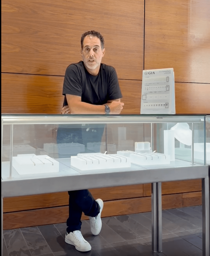 Brett Sandler with house of Milner Diamonds standing in front of a jewelry case with GIA rating card next to him