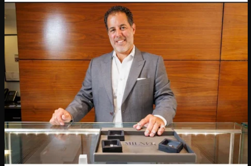 Brett Sandler in a suit standing behind a counter with a wooden wall in the background and diamonds on the counter